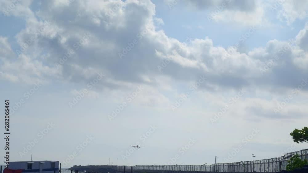 Civil jet airplane is landing on runway near beach on tropical island in cloudy weather with blue sky and sun Civil jet airplane is landing on runway near beach on tropical island in cloudy weather with blue sky and sun