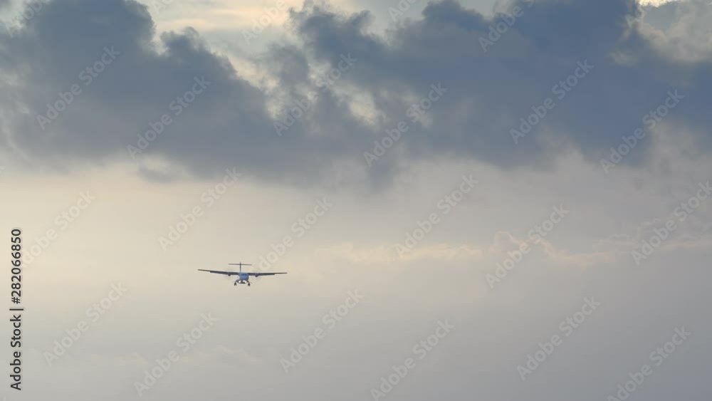 Small turboprop airplane is landing in sunset sky with yellow and blue dramatic clouds