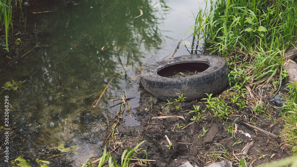 Garbage in the river or lake, the wheel is lying next to the water. The concept of environmental pollution, environmental problems of nature. Garbage in the river or lake, the wheel is lying next to the water. The concept of environmental pollution, environmental problems of nature.