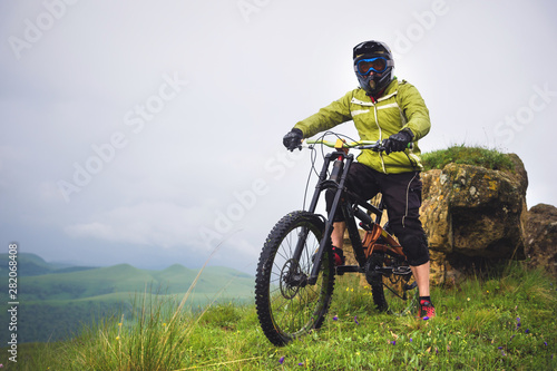Side view of a man on a mountain bike standing on a rocky terrain and looking at a rock. The concept of a mountain bike and mtb downhill