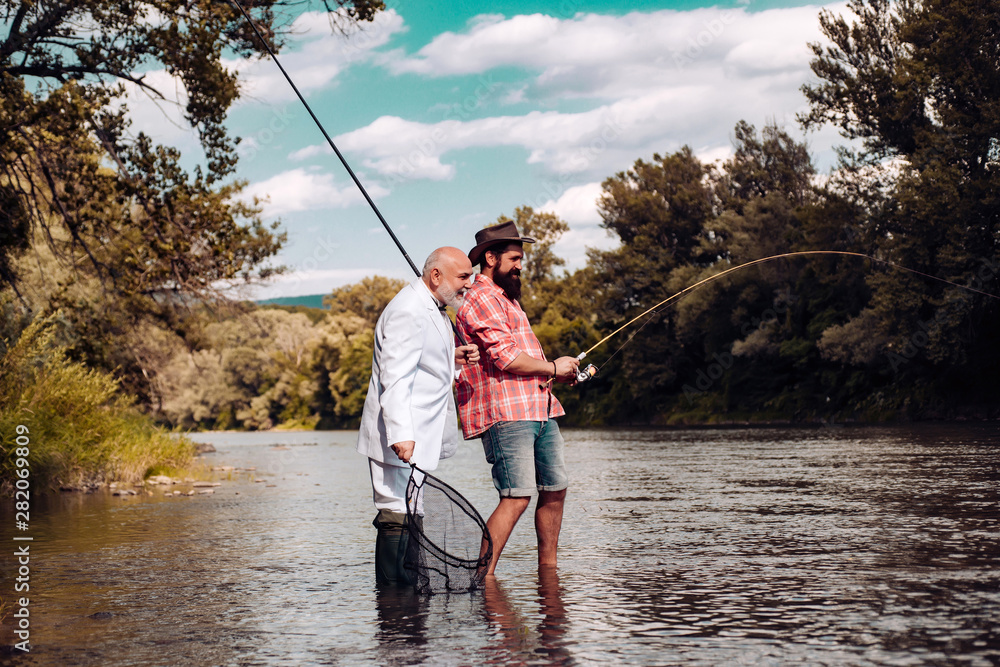 Fisherman fishing with spinning reel. Father and son fishing. Young man and old mature man fly fishing. Fishermen with fishing rod on the river.