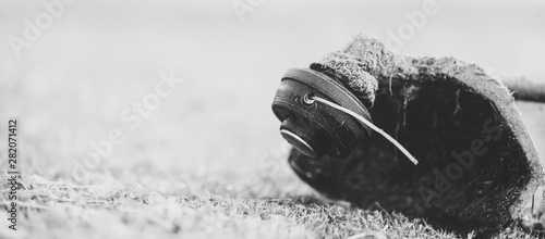 String trimmer on mown grass, close up. Theme of lawn care services, tool rental or repair. Banner format background with copy space. Monochrome with matte effect