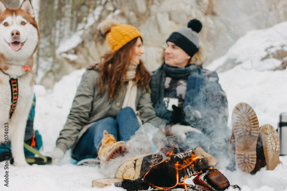 The happy couple with dog haski at the forest nature park in cold season, focus on fire. Travel adventure love story The happy couple with dog haski at the forest nature park in cold season, focus on fire. Travel adventure love story