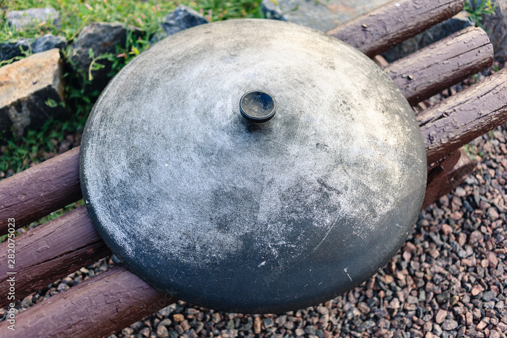 Cauldron lid on a wooden bench. Close-up image of a metal caldron lid. Cauldron lid on a wooden bench. Close-up image of a metal caldron lid.