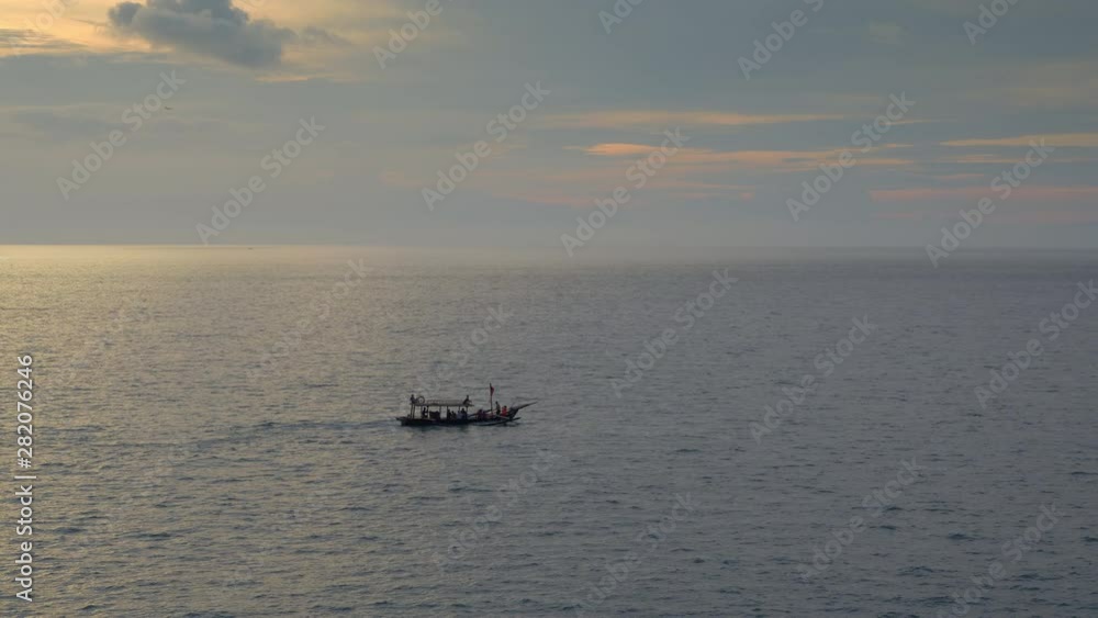 A small boat with people silhouettes is swimming in sea with beautiful dramatic sunset sky and airplane landing in background A small boat with people silhouettes is swimming in sea with beautiful dramatic sunset sky and airplane landing in background