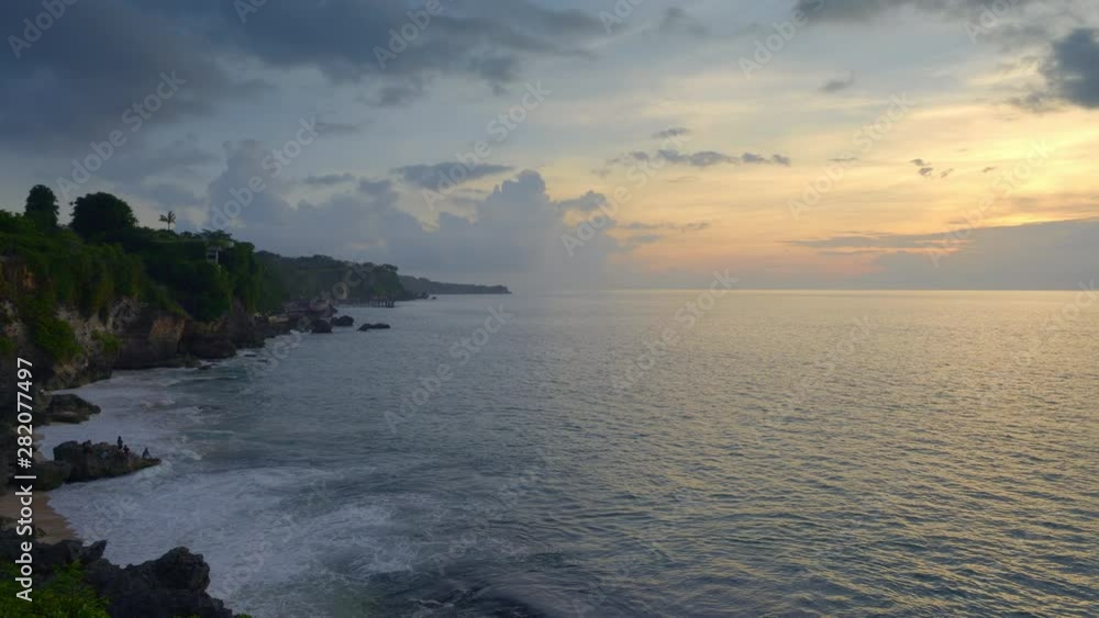 Tropical beach with people on rock and high tide waves during dark sunset sky in Bali island Tropical beach with people on rock and high tide waves during dark sunset sky in Bali island