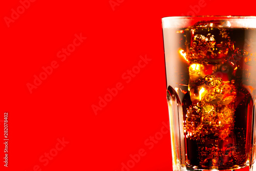 Coke with ice cubes closeup. Glass of fizzy brown drink over red background