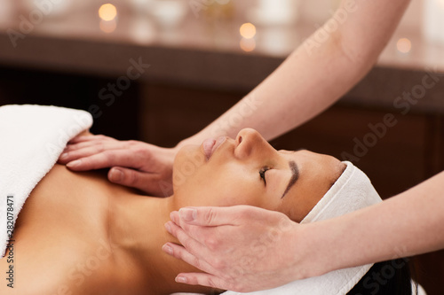 Side view of beautiful mixed-race woman enjoying face massage in luxury spa  copy space