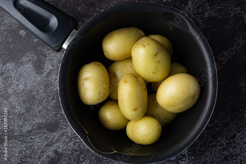 Raw potatoes in a pot on dark background. Selective focus.