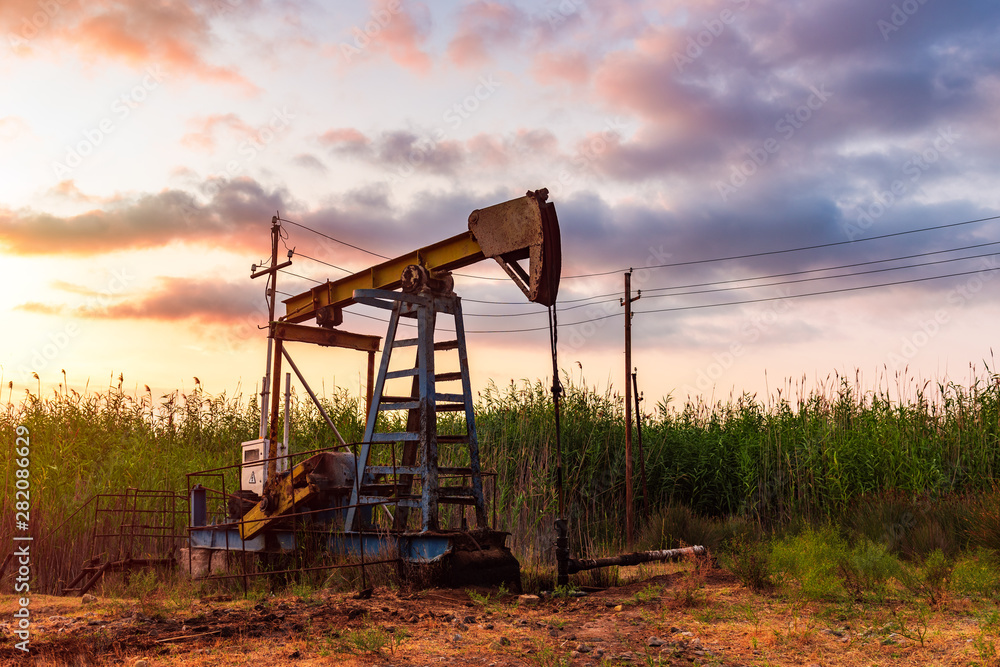 Oil rig pump against a colorful sunset sky