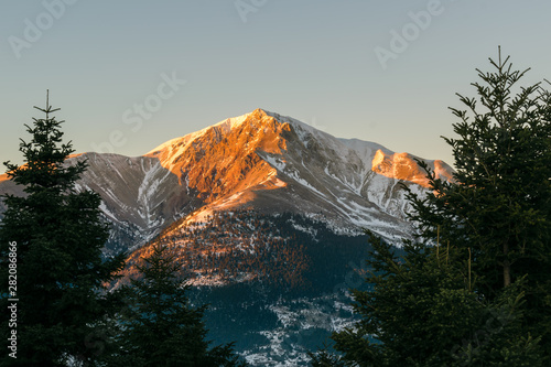 Velouchi mountain peak at sunset with fir trees in foreground and snow, Karpenisi photo