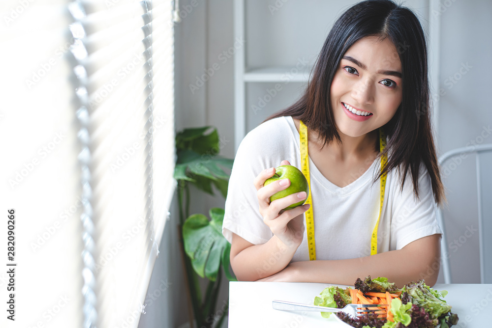 Beautiful women are healthy, holding an apple in hand. And a plate of salad on the table. Diet, Clean food, Healthy food concept. Beautiful women are healthy, holding an apple in hand. And a plate of salad on the table. Diet, Clean food, Healthy food concept.