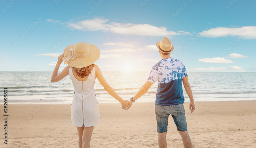 Young happy couple on seashore. Vacation couple walking on beach together in love holding around each other. Happy interracial young couple. Asian woman and caucasian man Young happy couple on seashore. Vacation couple walking on beach together in love holding around each other. Happy interracial young couple. Asian woman and caucasian man