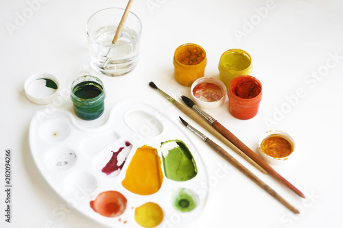 Gouache multi-colored paints, brushes, palette and a glass of water for brushes on a white background