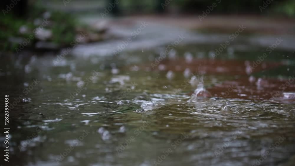 Close-up raindrops falling in puddle over paved walkway at city street making bubbles during heavy autumn rain. Fall weather forecast. Close-up raindrops falling in puddle over paved walkway at city street making bubbles during heavy autumn rain. Fall weather forecast.