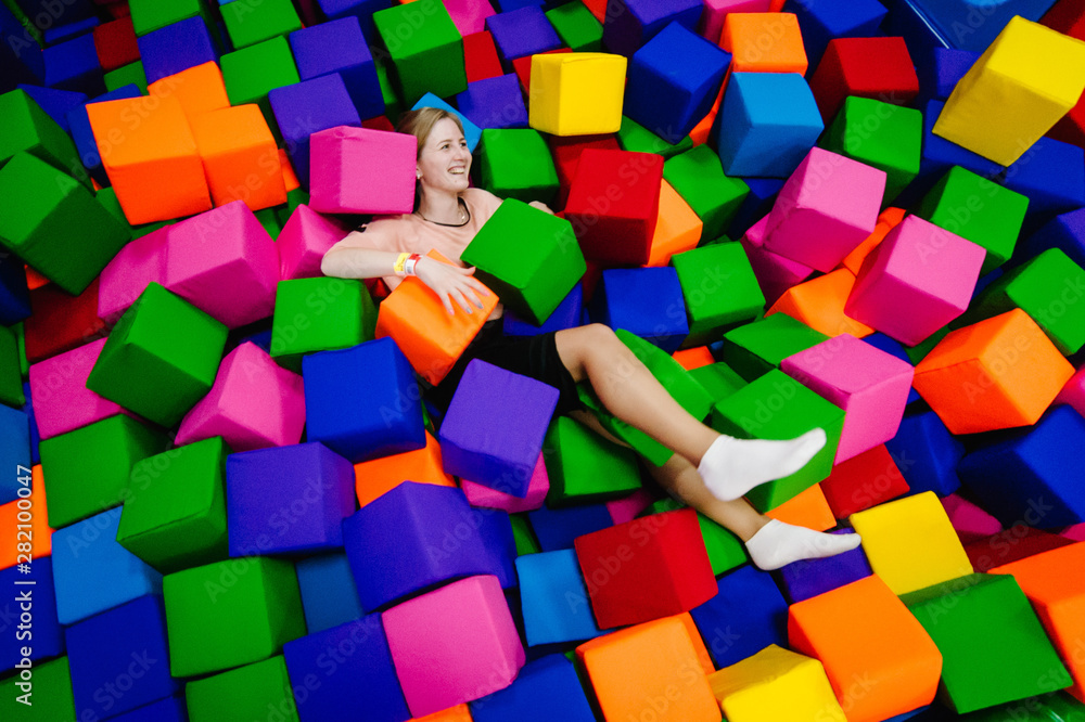 Obraz premium A young woman or girl, mother playing and jumping in soft cubes in the dry pool of the game children's room for birthday. entertainment centre. indoor playground in foam rubber pit in trampoline.