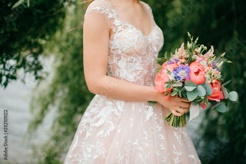 Beautiful young bride in white wedding dress posing outdoor with bouquet of flowers.