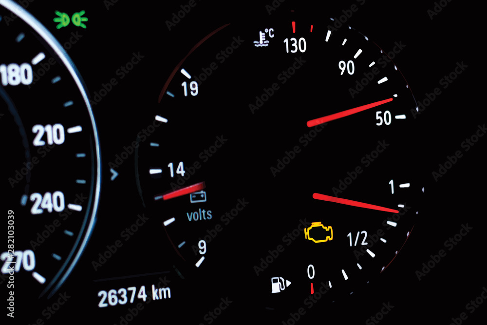 Illustration of selective focus of malfunction check engine warning light on car dashboard. Side view of modern car instrument panel with odometer, car water temperature, car voltmeter and fuel gauge.