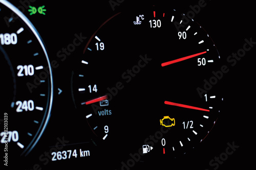 Illustration of selective focus of malfunction check engine warning light on car dashboard. Side view of modern car instrument panel with odometer, car water temperature, car voltmeter and fuel gauge.