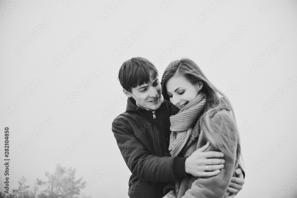 People, season, love and leisure concept - happy young couple hugging and laughing outdoors in winter. Man and woman walk in snow park. Black and white photo.