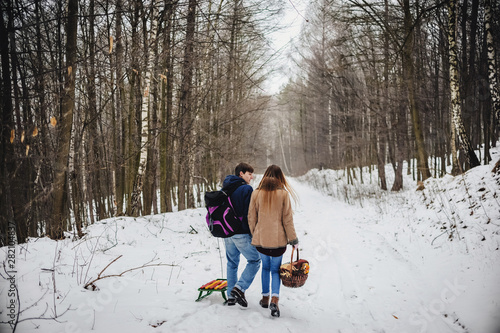 Beautiful young couple on a walk back pulling sledge, winter day. Happy holidays. Merry christmas and happy new year concept.
