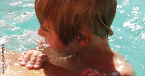 Young boy holding into swimming poolside