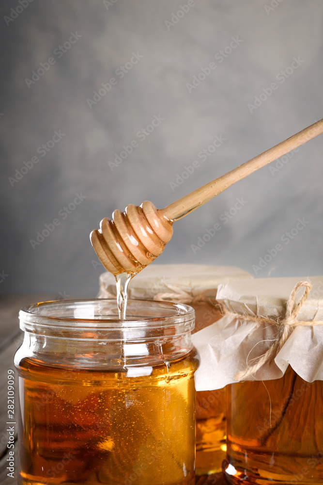 Pouring aromatic honey into jar, closeup. Honey in glass jars and honeycombs wax on wooden background. Wooden stick , instruments Pouring aromatic honey into jar, closeup. Honey in glass jars and honeycombs wax on wooden background. Wooden stick , instruments