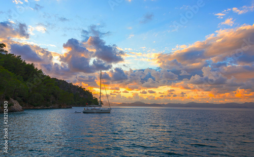 Sailing yacht in the bay against the backdrop of a bright multicolour sunset.
