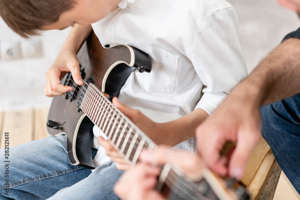 Fototapeta premium Young boy moves his hand along guitar strings while his father helps boy to take chords