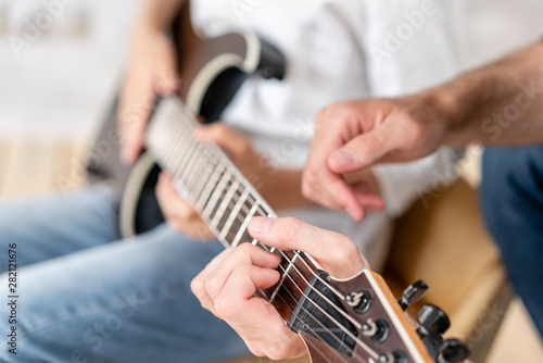 Adult man helps his little brother to learn how to play elecrtric guitar