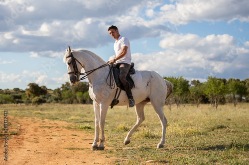 Young guy in casual outfit riding white horse on meadow a sunny day  © pablobenii