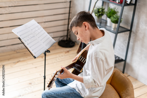 Focused kid playing his favorite melody on acoustic guitar