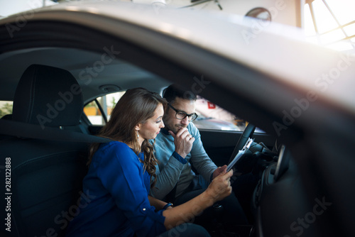 Happy couple sitting inside brand new car they want to buy and discussing about the pricing.