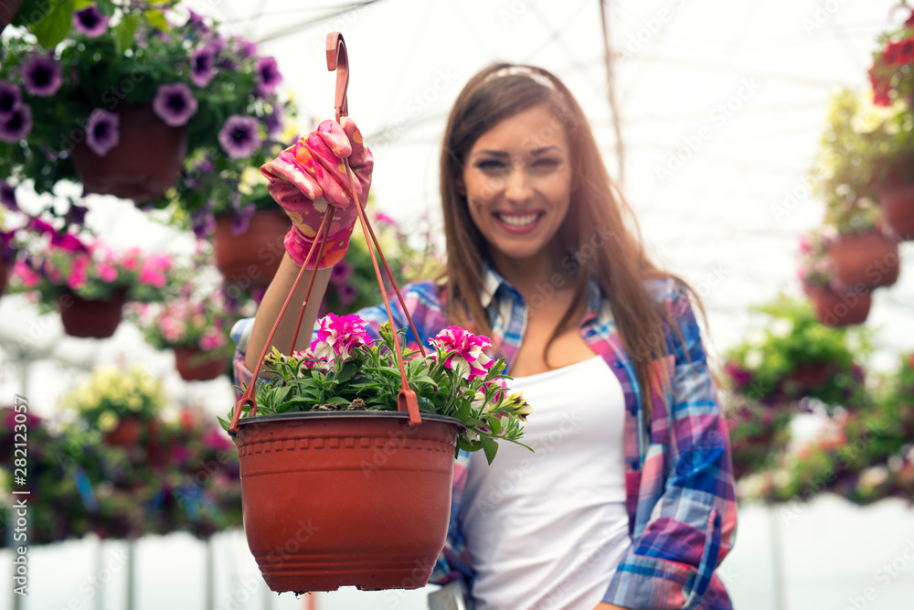 Happy smiling woman florist working holding potted flowers in greenhouse garden. Focus on potted plants.