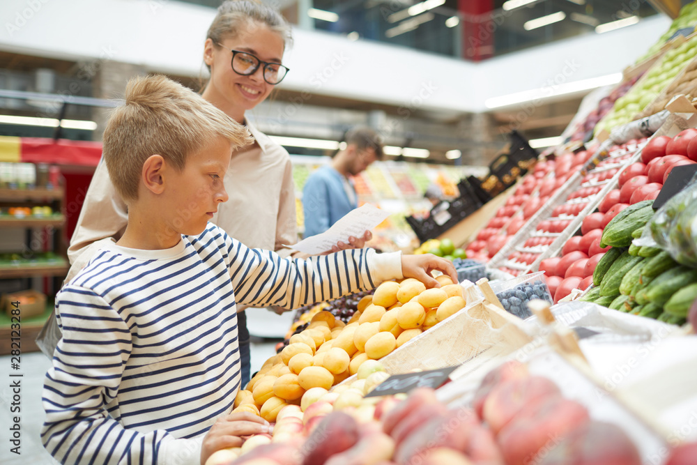 Side view portrait of teenage boy choosing fresh fruits at farmers market while grocery shopping with family, copy space