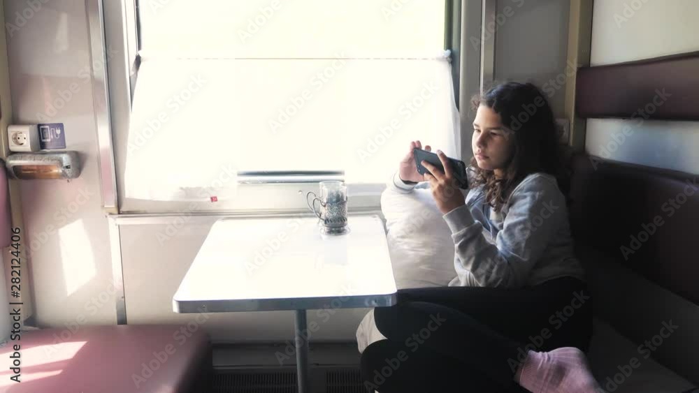 little girl walks on a train compartment car with and a smartphone. travel transportation railroad concept. the girl in the train at the window corresponds the girl in the train wagon at the window little girl walks on a train compartment car with and a smartphone. travel transportation railroad concept. the girl in the train at the window corresponds the girl in the train wagon at the window