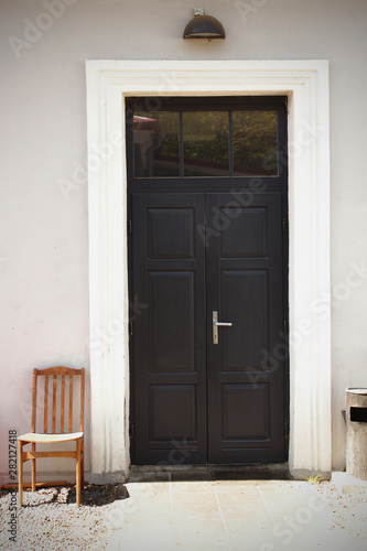 Old wooden chair in a yard near the black entrance door