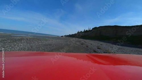 POV over the hood of a red off-road 4x4 vehicle while driving north along a desolate beach  towards a large boulder on the beach near Ninilchik, Alaska photo