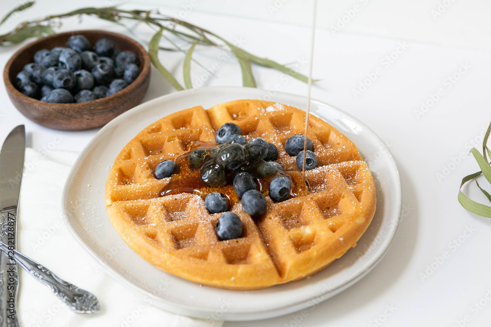 Maple Syrup pouring on Belgian waffle with blueberries, Dusted with Powdered Sugar, White Background, Copy Space Maple Syrup pouring on Belgian waffle with blueberries, Dusted with Powdered Sugar, White Background, Copy Space