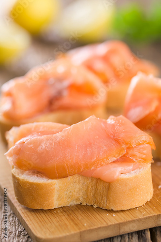 Smoked salmon slices on baguette on wooden board (Selective Focus, Focus one third into the image)