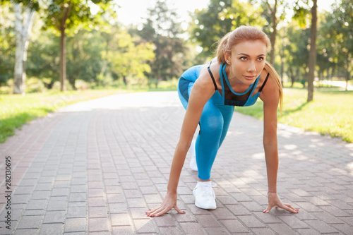 Beautiful athletic woman in starting position, ready to sprint, copy space. Attractive sportswoman working out outdoors in the park
