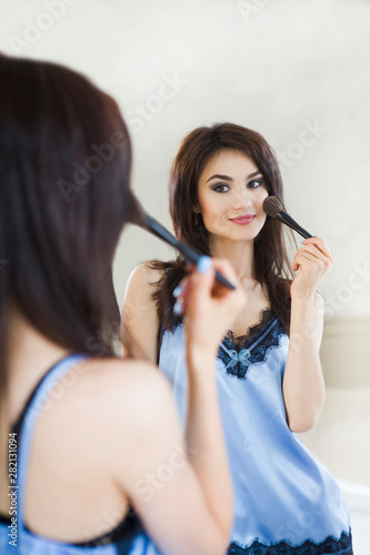 Young woman in a pajamas applying make-up looking in a mirror