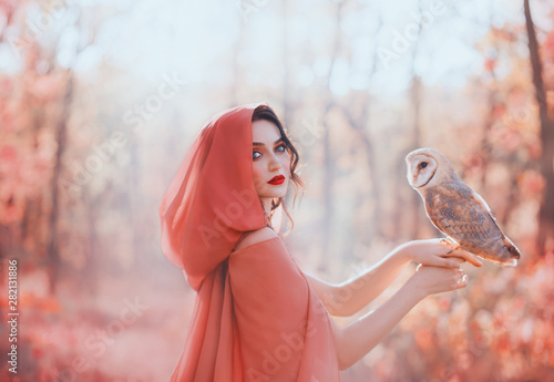 Canvastavla mystical pagan woman with covered head in peach scarf in forest, holds cute little barn owl