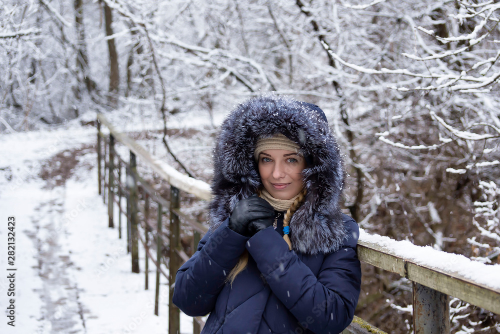 A cute, young, beautiful girl in a blue warm coat with a hood decorated with fur walks in a snowy, winter park. A cute, young, beautiful girl in a blue warm coat with a hood decorated with fur walks in a snowy, winter park.