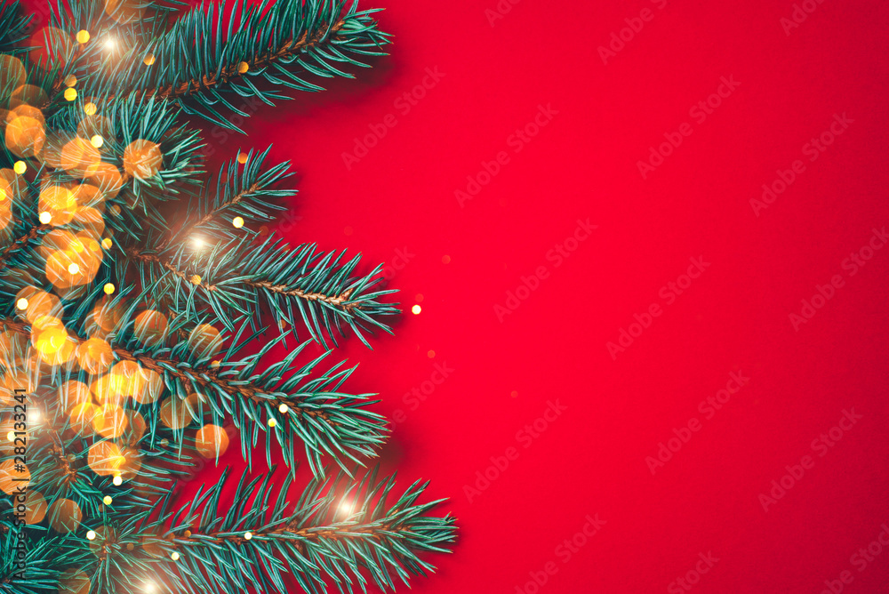 Fir branches with blurred lights garland on a red background. Christmas wallpaper. Flat lay, copy space.