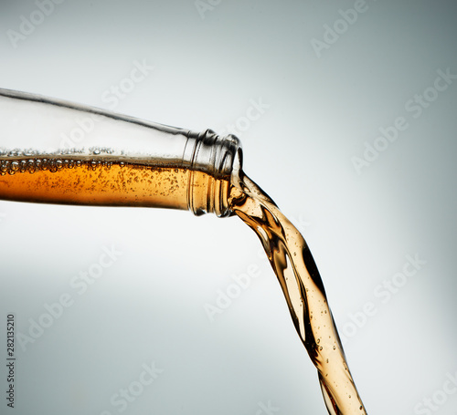 Hard cider poured from clear bottle. Stop action closeup on grey background