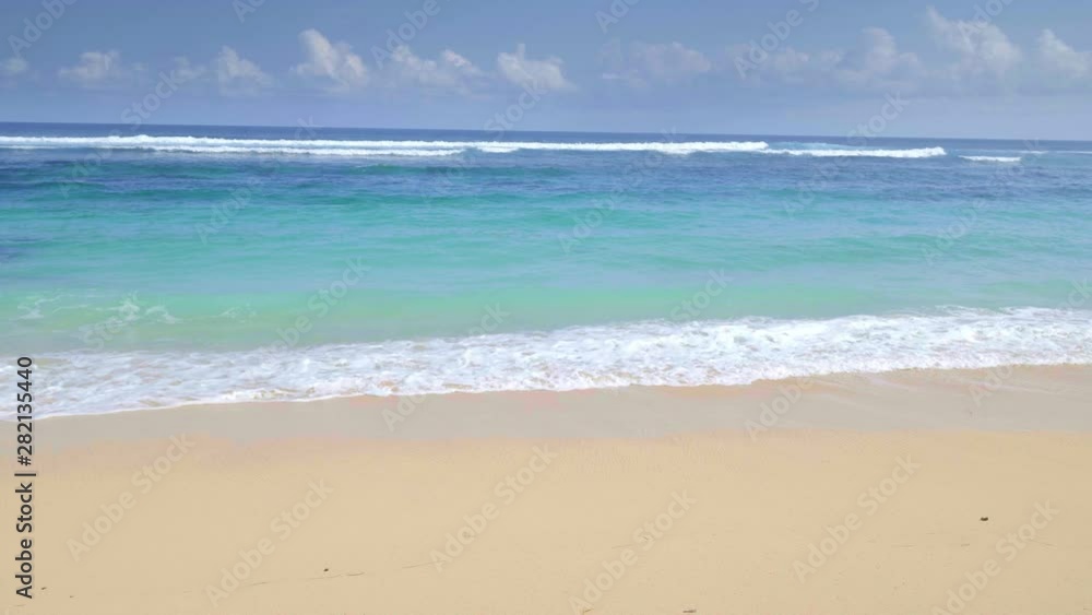 A panoramic shot of tropical sandy beach and rocks with colorful blue water and waves filmed in slow motion A panoramic shot of tropical sandy beach and rocks with colorful blue water and waves filmed in slow motion