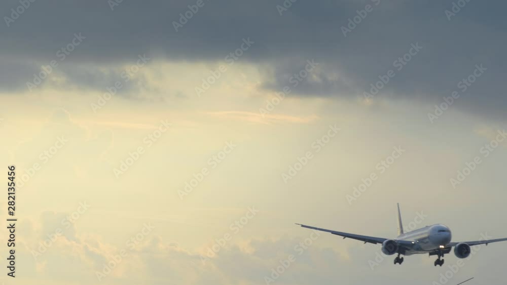 Close up of big airplane is landing in yellow sunset sky with dramatic clouds Close up of big airplane is landing in yellow sunset sky with dramatic clouds