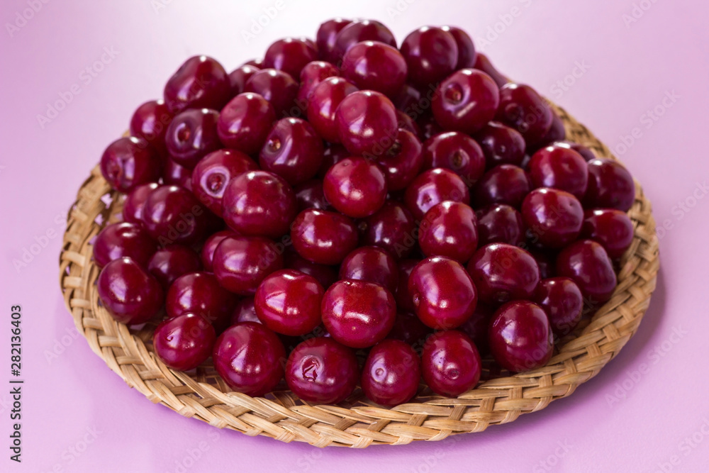 Cherry berries on a plate of wicker straws. Pink background Cherry berries on a plate of wicker straws. Pink background