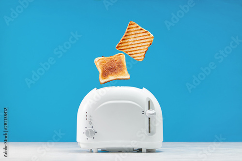 Roasted toast bread popping up of toaster with blue wall